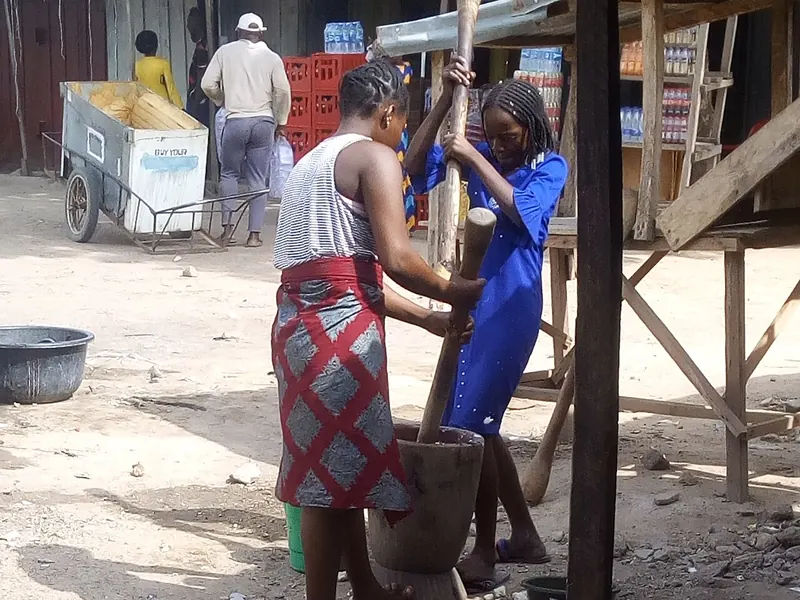 Two people pounding boiled yam in a wooden mortar with a long pestle
